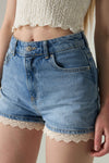 Denim shorts with lace trim worn by a person, against a neutral background.