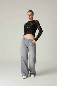 Person wearing a black lace top and gray jeans on a plain background.