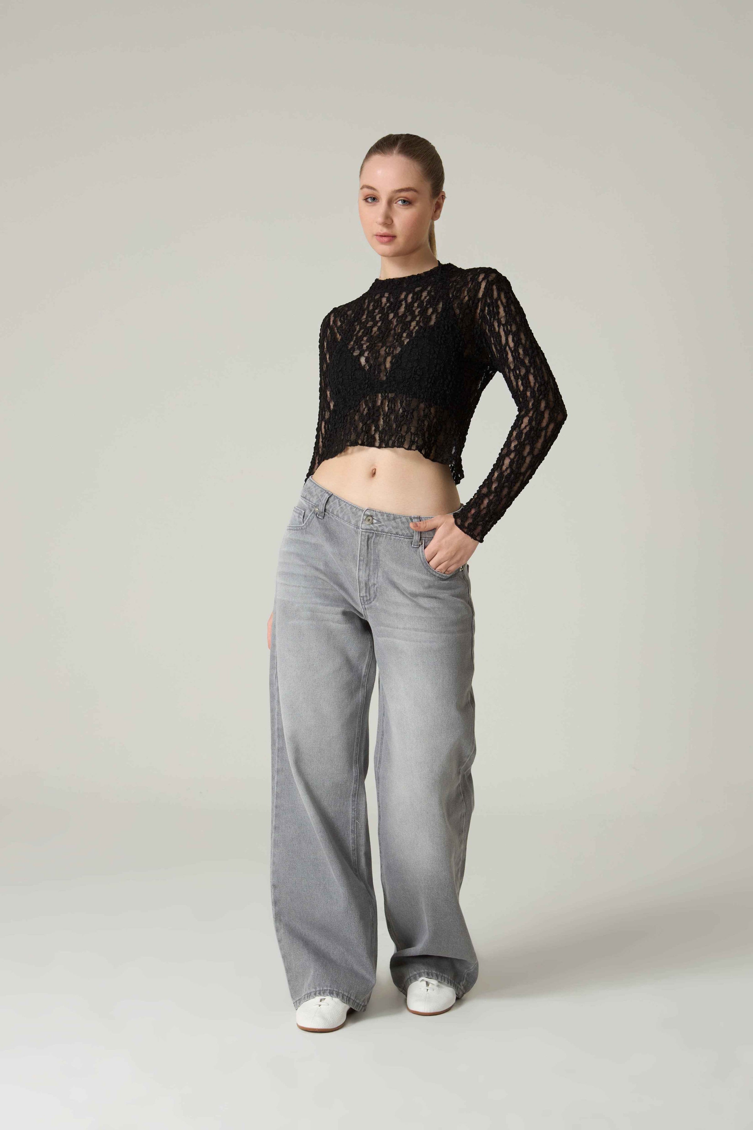 Person wearing a black lace top and gray jeans on a plain background.