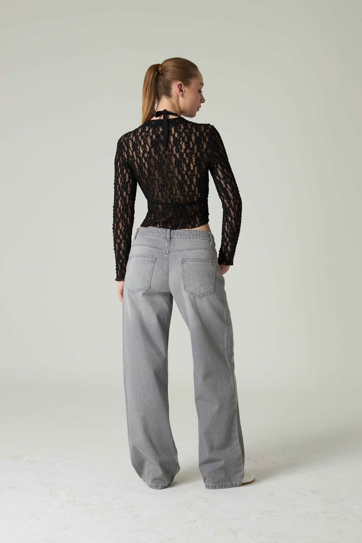 Person wearing a black lace top and gray pants on a white background.