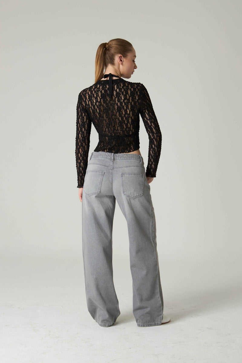 Person wearing a black lace top and gray pants on a white background.