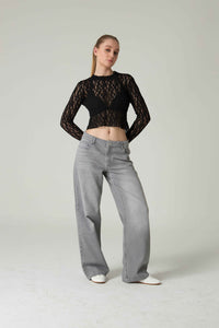 Person wearing a black lace top and gray jeans on a plain background.