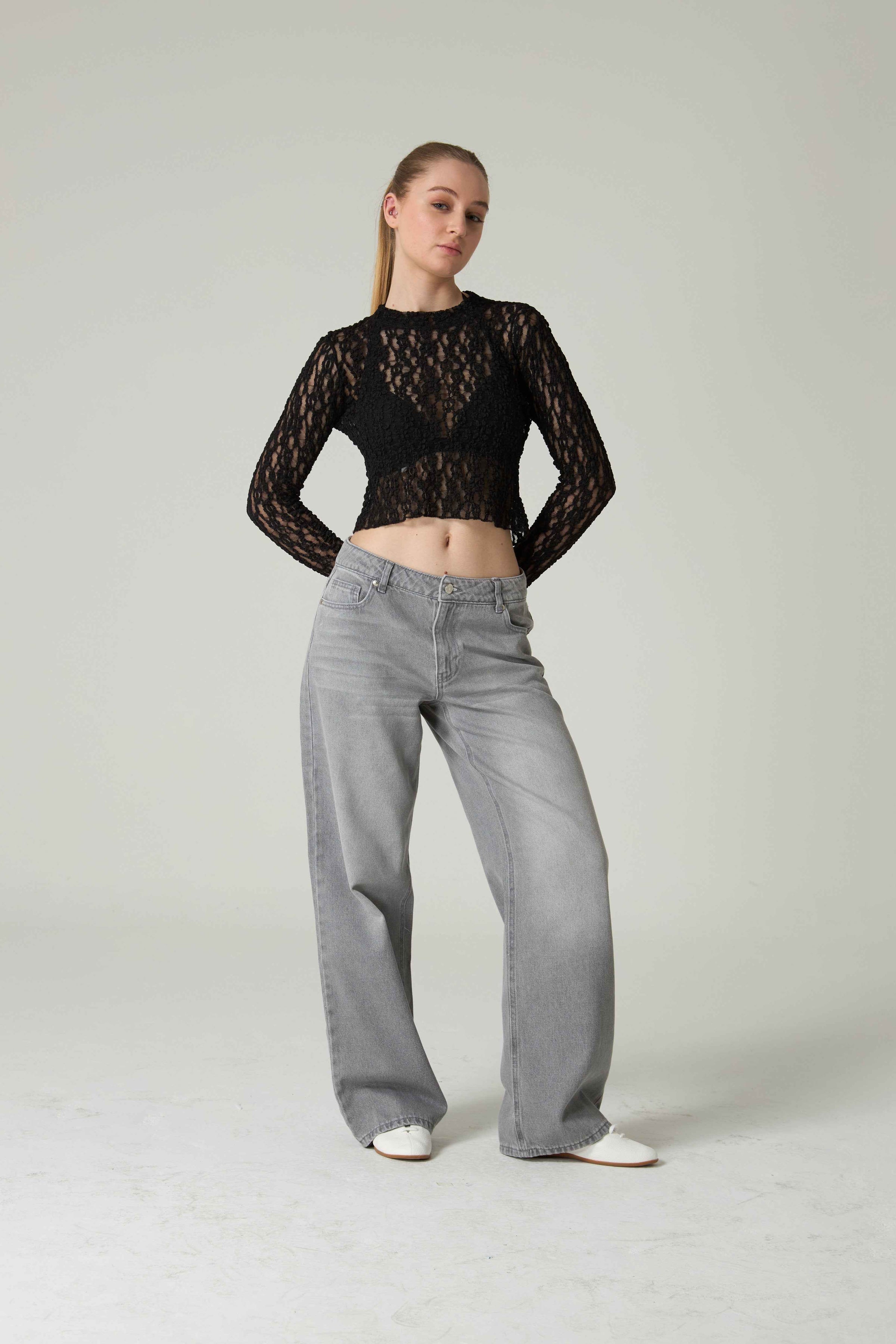 Person wearing a black lace top and gray jeans on a plain background.