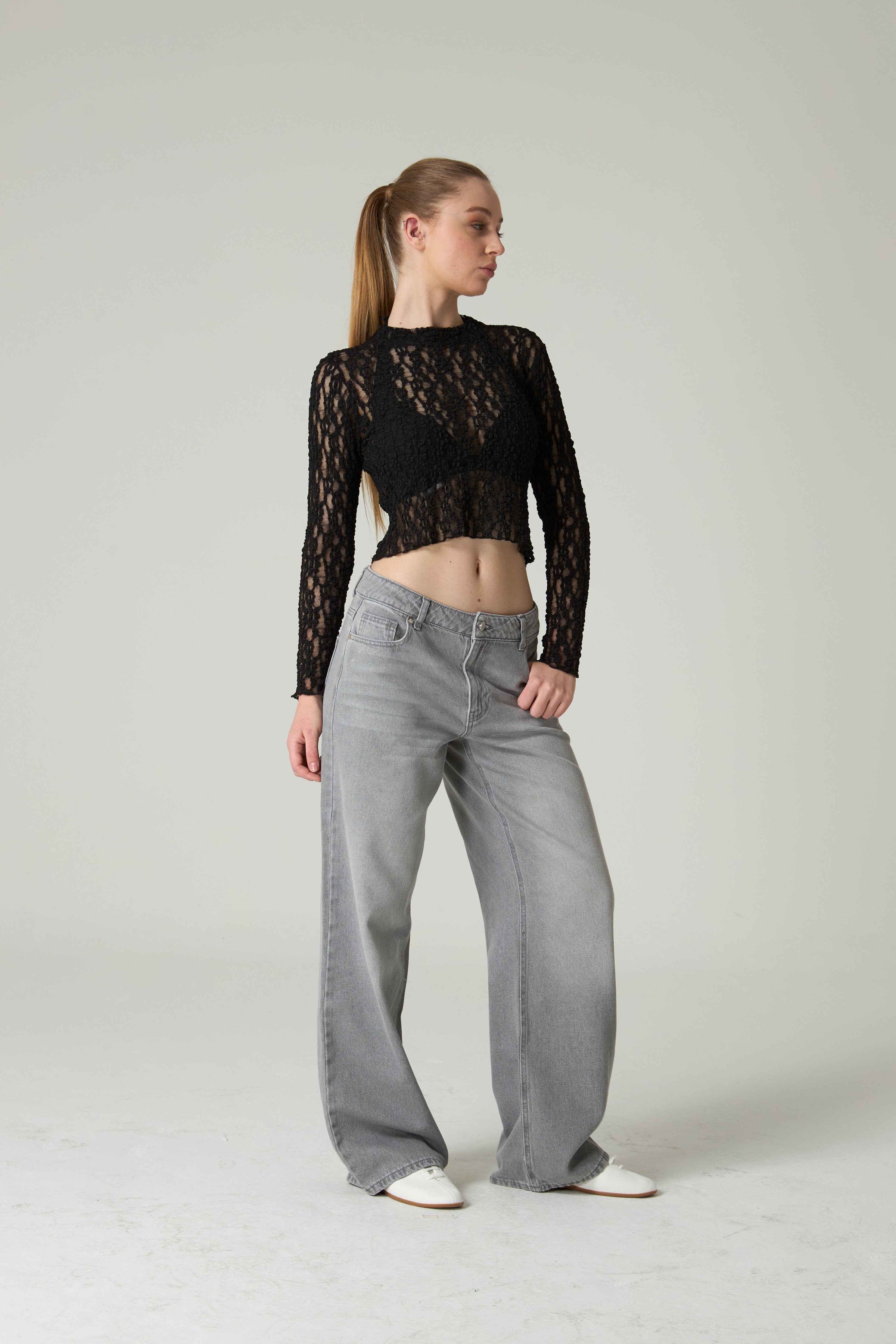 Person wearing a black lace top and gray jeans on a plain background.