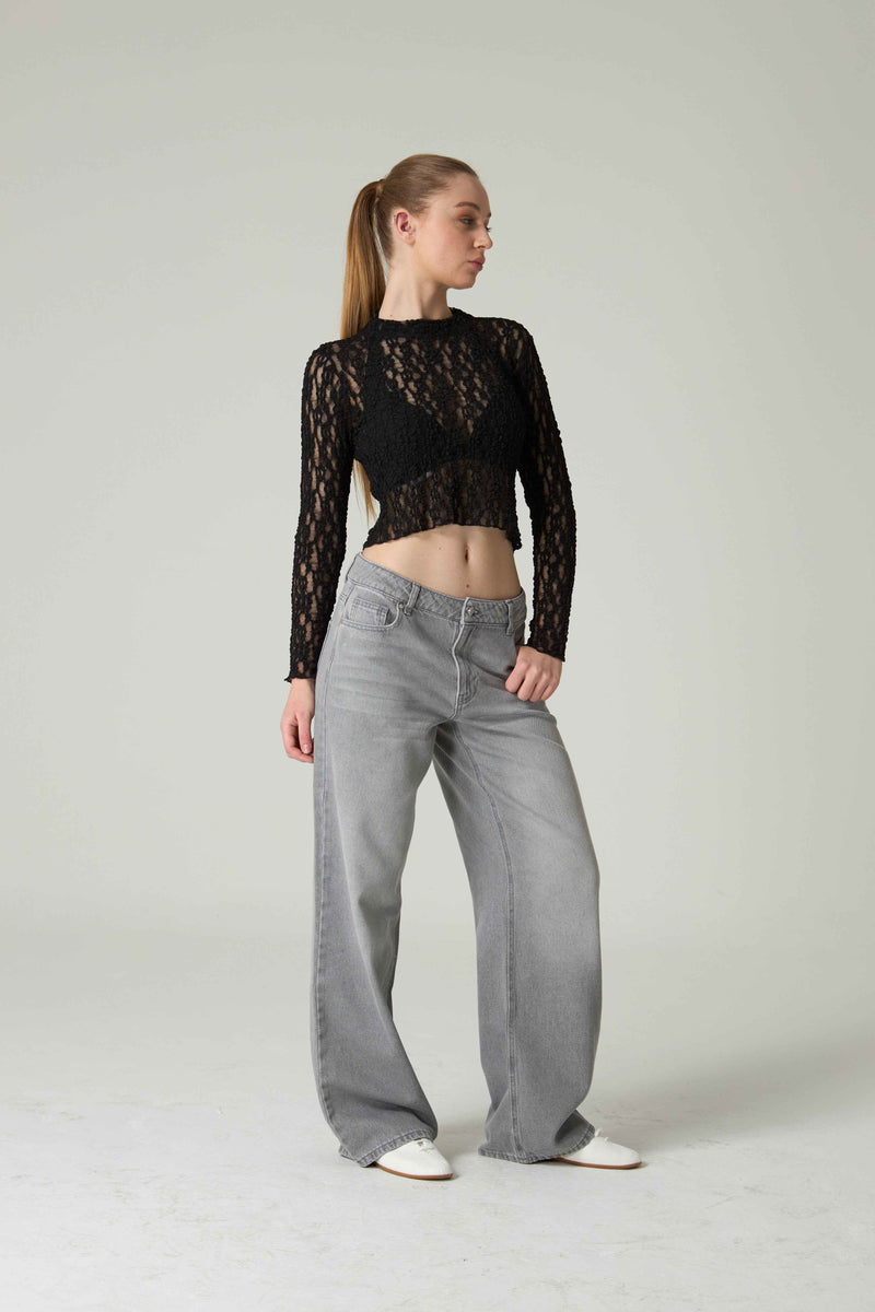Person wearing a black lace top and gray jeans on a plain background.