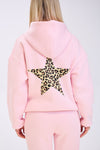 Back view of a woman wearing a light pink hoodie with a large leopard print star design on the back, paired with matching pink sweatpants, against a plain white background.