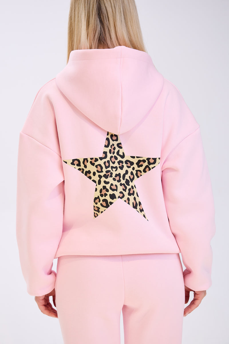 Back view of a woman wearing a light pink hoodie with a large leopard print star design on the back, paired with matching pink sweatpants, against a plain white background.