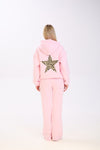 Back view of a woman wearing a pastel pink hoodie with a large leopard print star on the back, paired with matching wide-leg pink pants, standing against a plain white background.