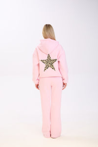 Back view of a woman wearing a pastel pink hoodie with a large leopard print star on the back, paired with matching wide-leg pink pants, standing against a plain white background.