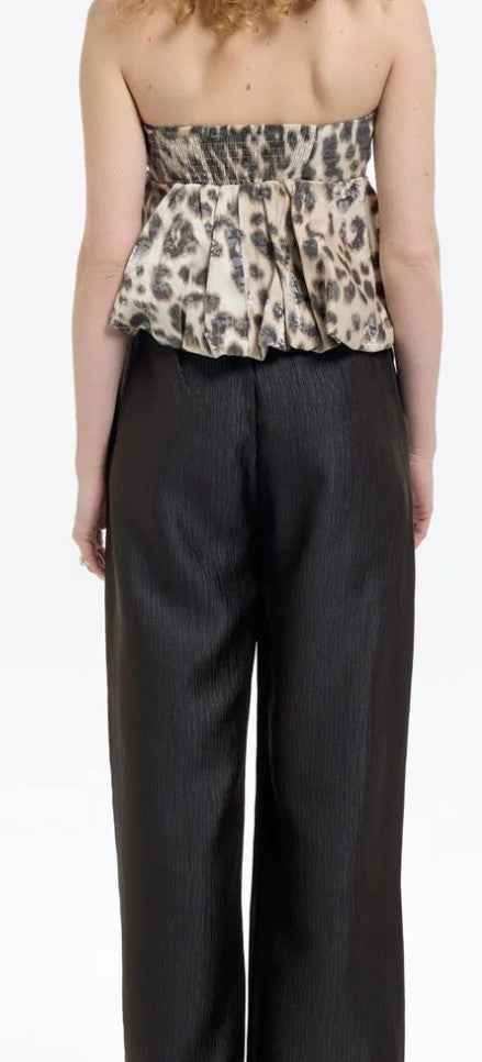 Woman wearing a leopard print strapless top and black pants on a white background.