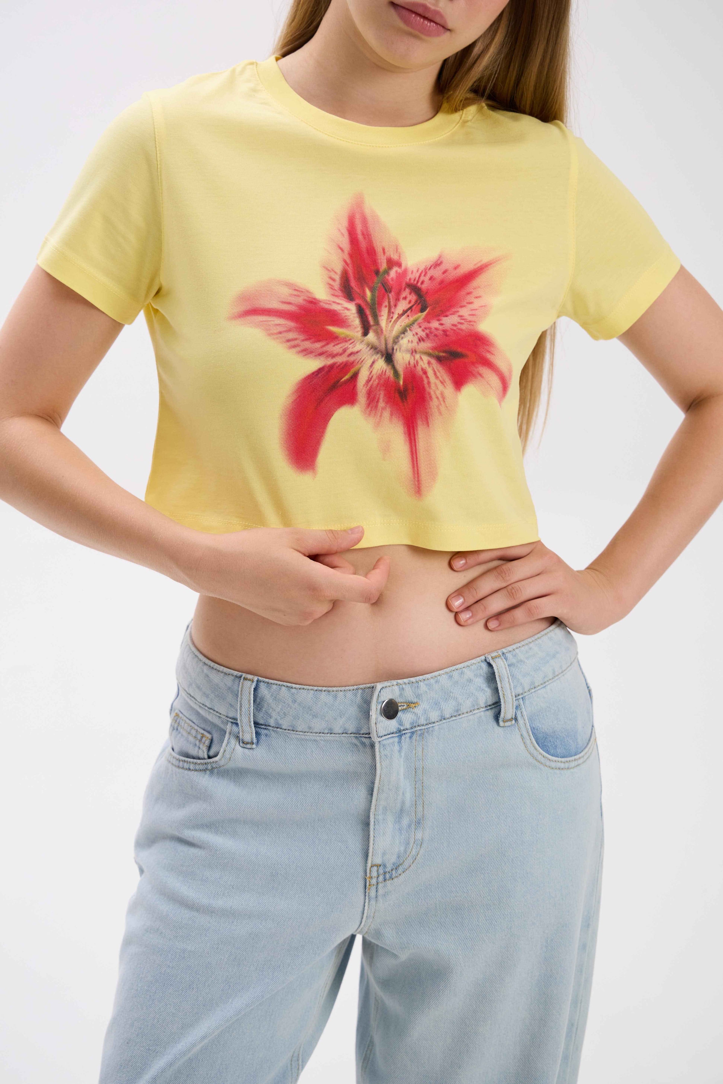 Person wearing a yellow t-shirt with a red floral design and light blue jeans on a white background.