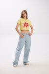 Person wearing a yellow t-shirt with a red flower design and light blue jeans on a white background.