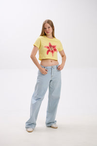 Person wearing a yellow t-shirt with a red flower design and light blue jeans on a white background.