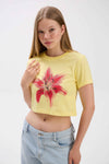 Woman wearing a yellow crop top with a red floral design on a white background.