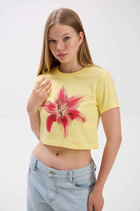 Woman wearing a yellow crop top with a red floral design on a white background.