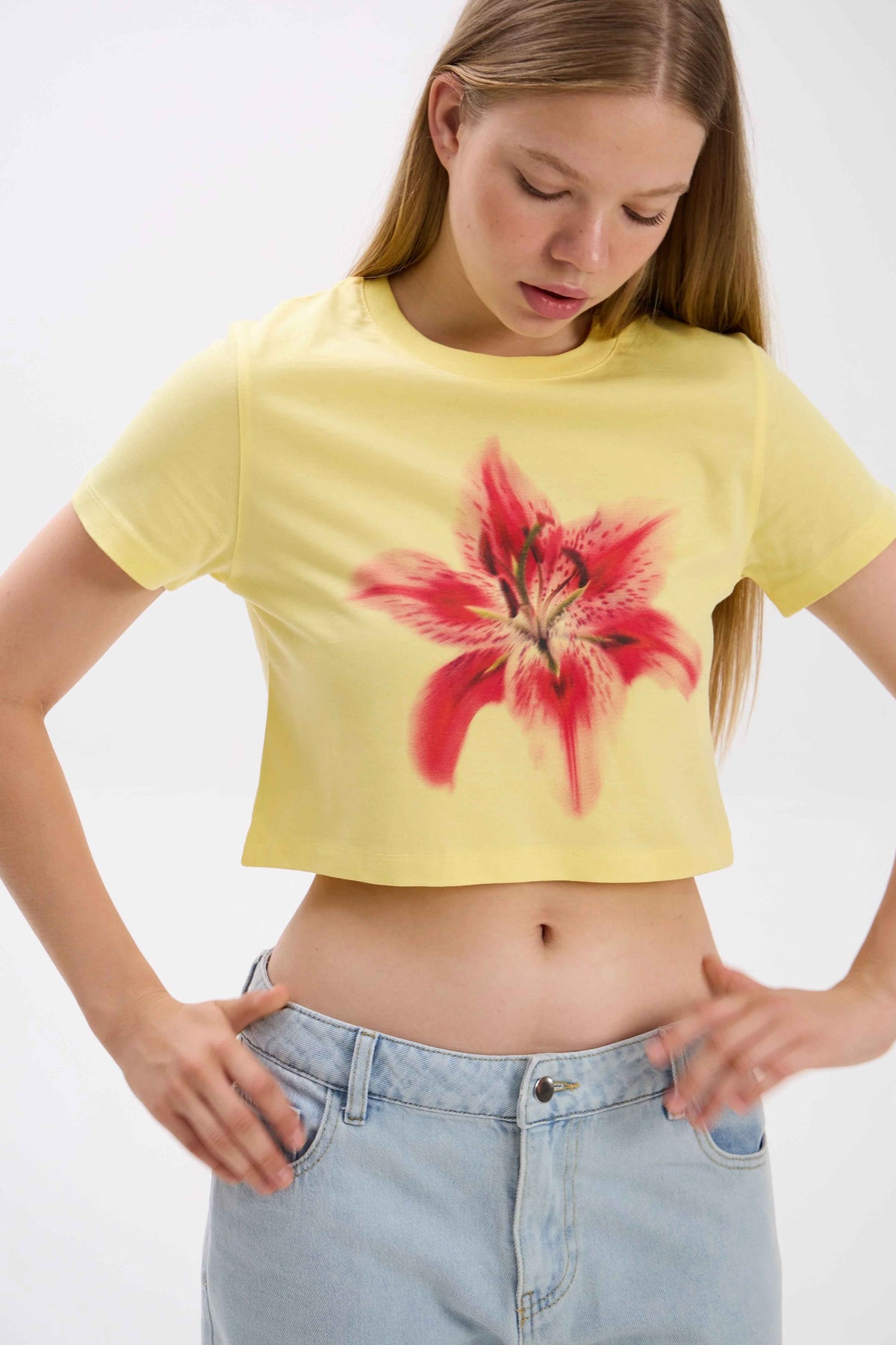 Person wearing a yellow crop top with a red floral design and light blue jeans on a white background.