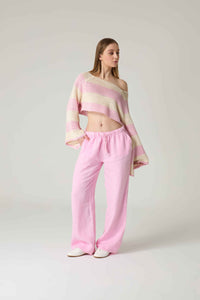 Woman wearing a pink and white striped sweater and pink pants on a light gray background.