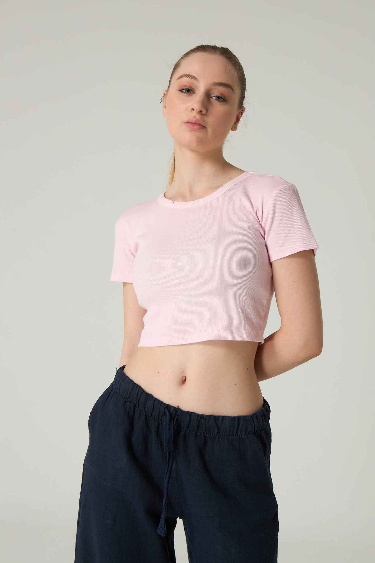 Person wearing a pink crop top and dark pants on a plain background.