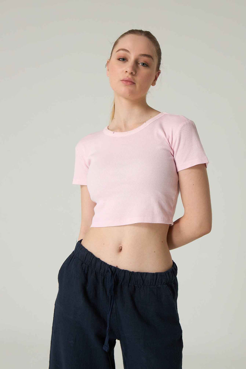 Person wearing a pink crop top and dark pants on a plain background.