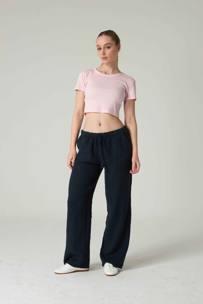Woman wearing a pink crop top and navy pants on a white background.