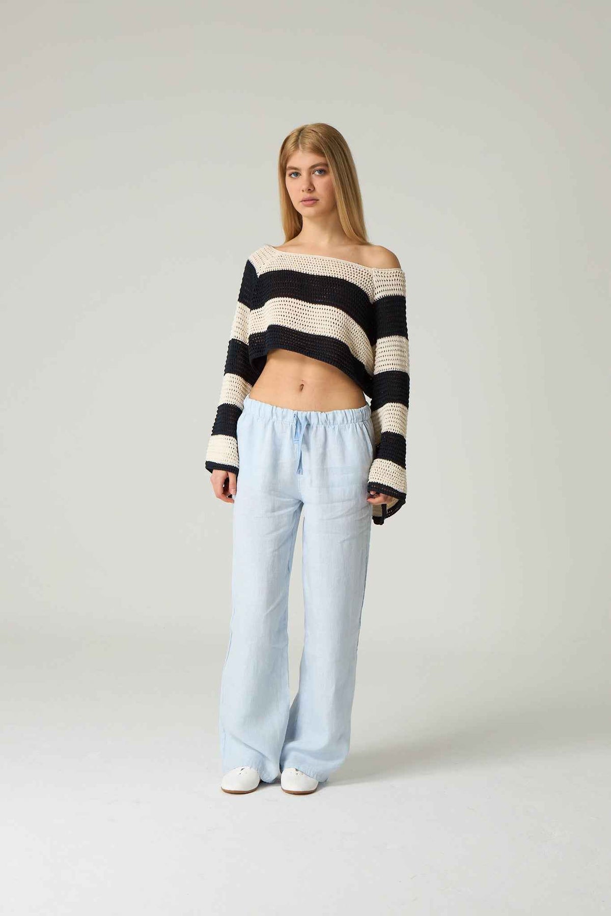 Woman wearing a black and white striped sweater and light blue pants on a plain background.