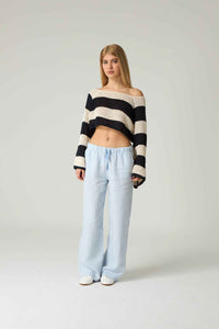 Woman wearing a black and white striped sweater and light blue pants on a plain background.