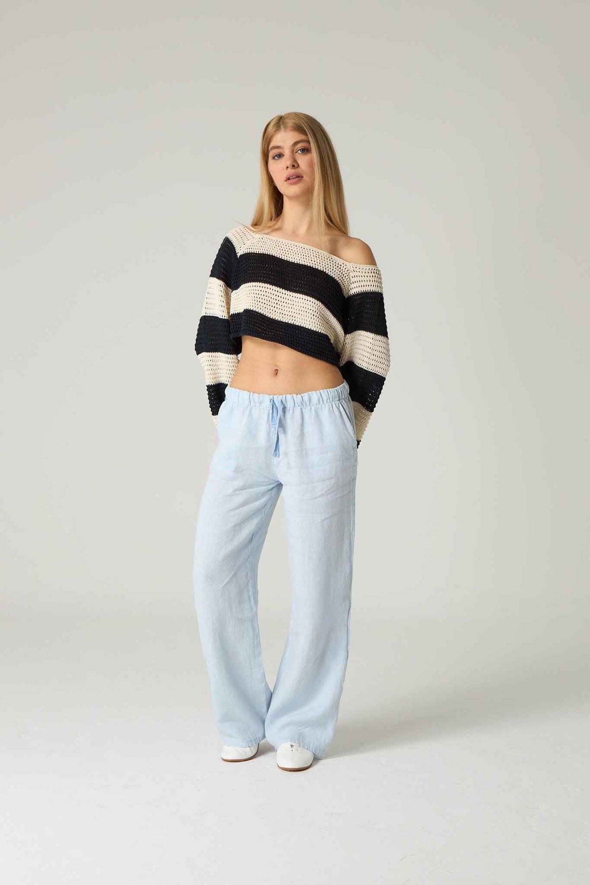 Woman wearing a black and white striped sweater and light blue pants on a plain background.