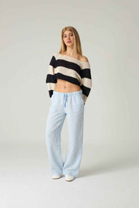 Woman wearing a black and white striped sweater and light blue pants on a plain background.