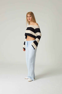 Woman wearing a black and white striped sweater with light blue jeans on a plain background.