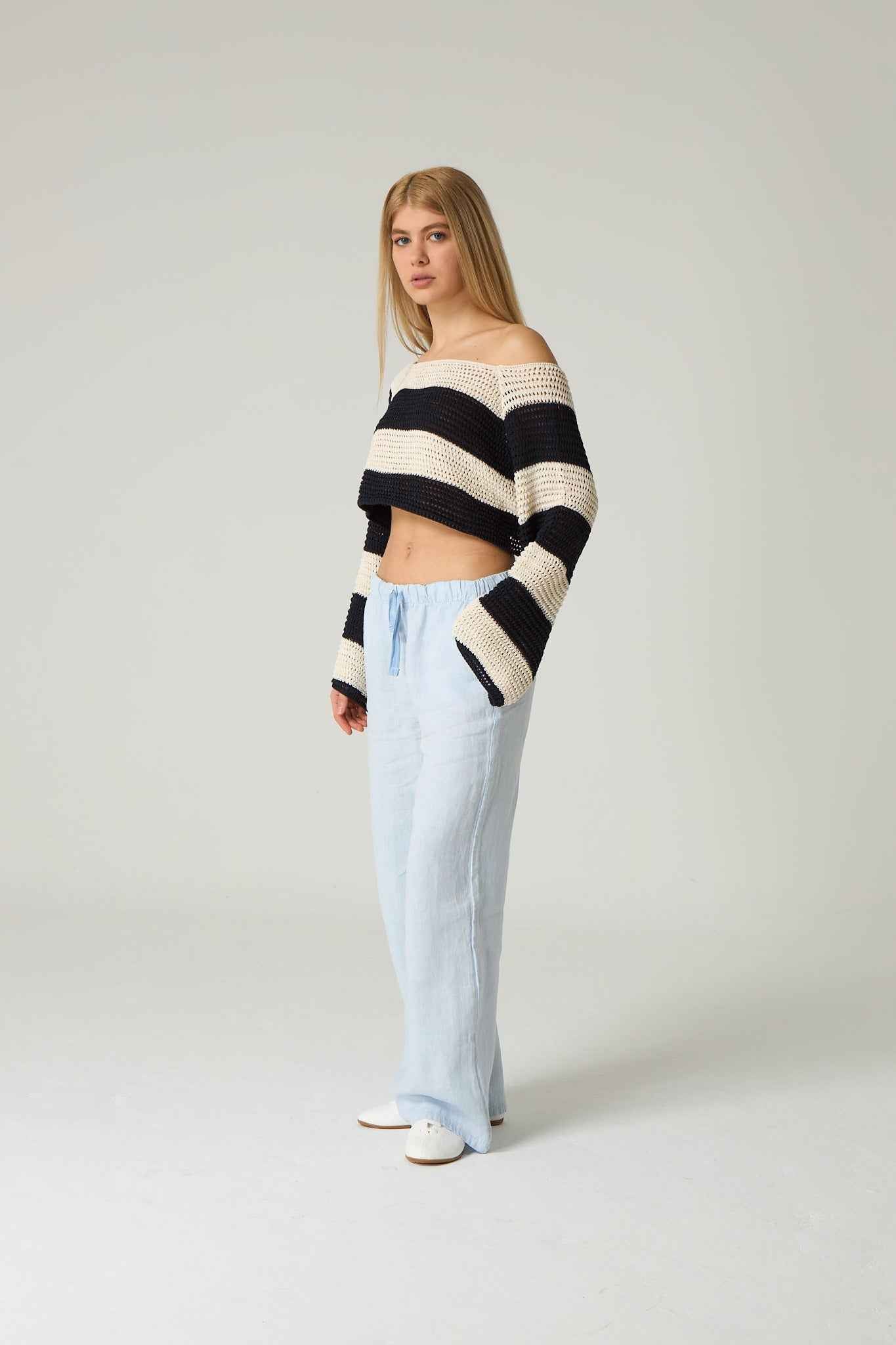 Woman wearing a black and white striped sweater with light blue jeans on a plain background.