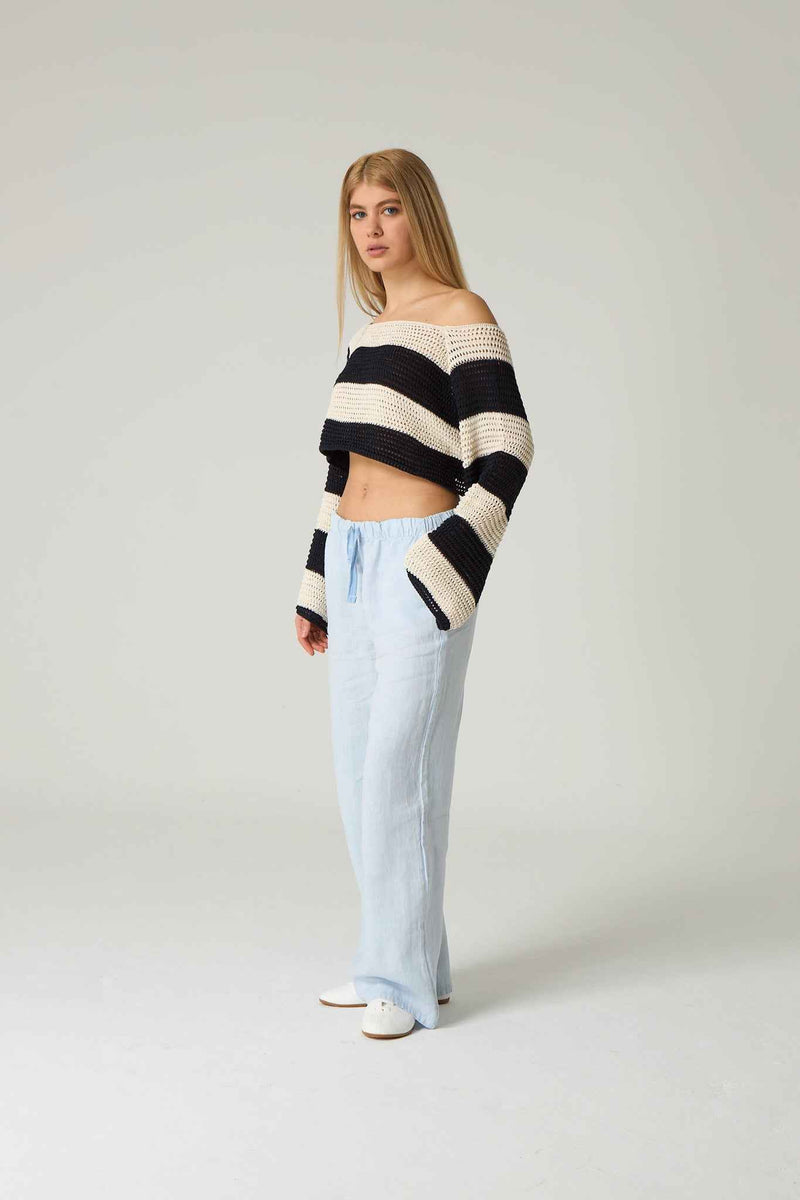 Woman wearing a black and white striped sweater with light blue jeans on a plain background.