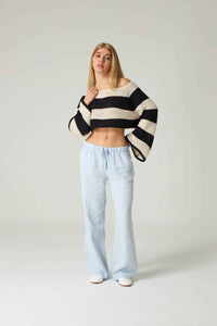 Person wearing a black and white striped sweater and light blue jeans on a plain background.