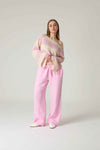Woman wearing a pink and white striped sweater and pink pants on a white background.
