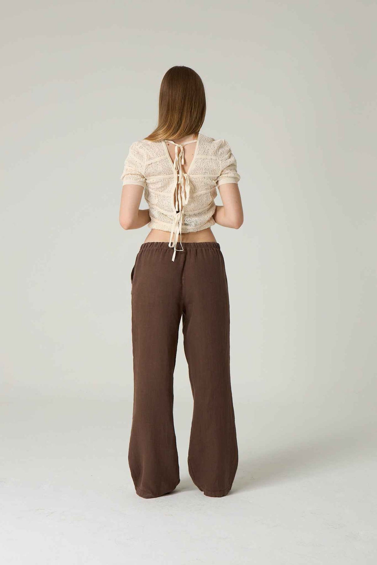 Woman wearing a beige top and brown pants on a plain background.