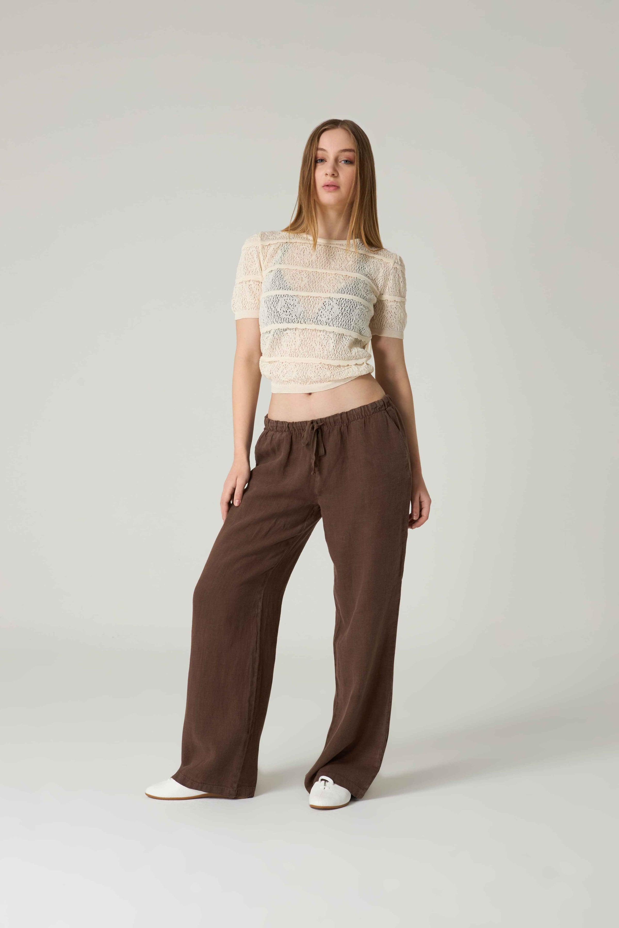 Woman wearing a striped top and brown pants on a plain background.