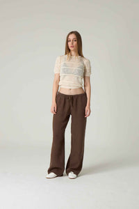 Woman wearing a sheer top and brown pants on a plain background.