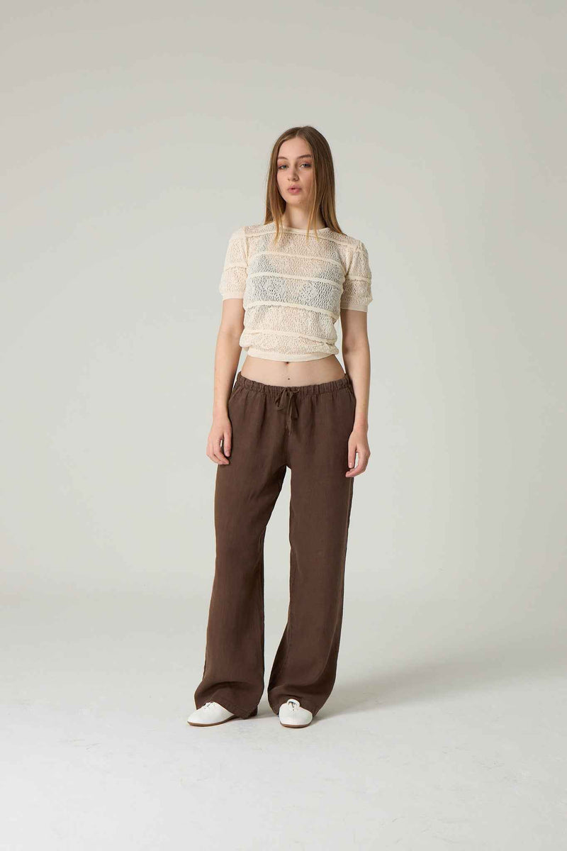 Woman wearing a sheer top and brown pants on a plain background.