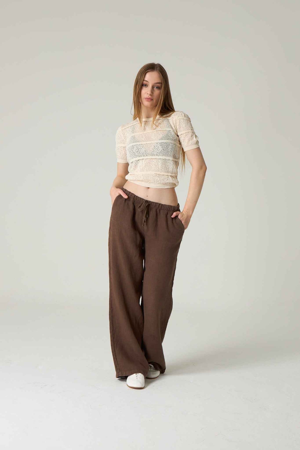 Woman wearing a white top and brown pants on a plain background.