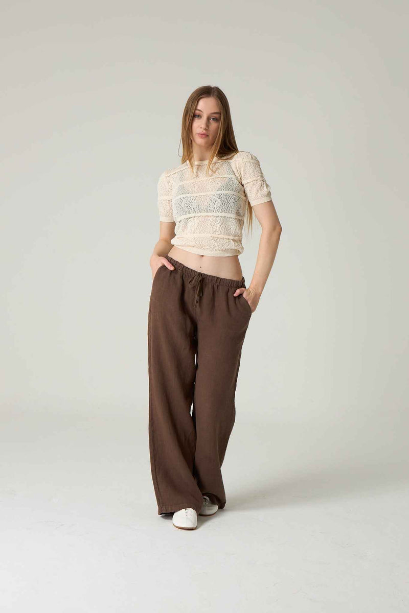 Woman wearing a white top and brown pants on a plain background.