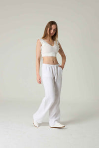 Woman wearing a white crochet top and white pants on a plain background.