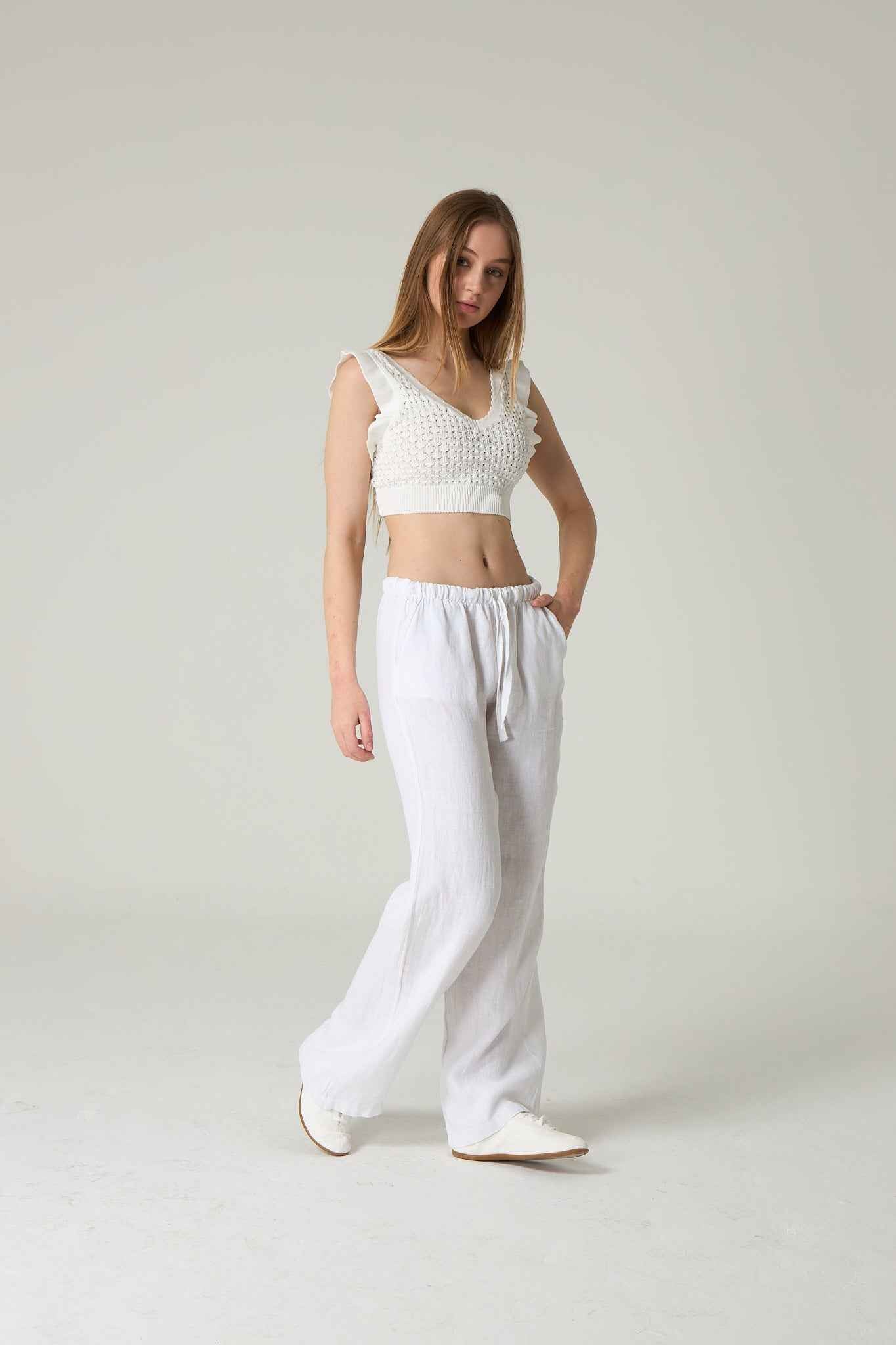 Woman wearing a white crochet top and white pants on a plain background.