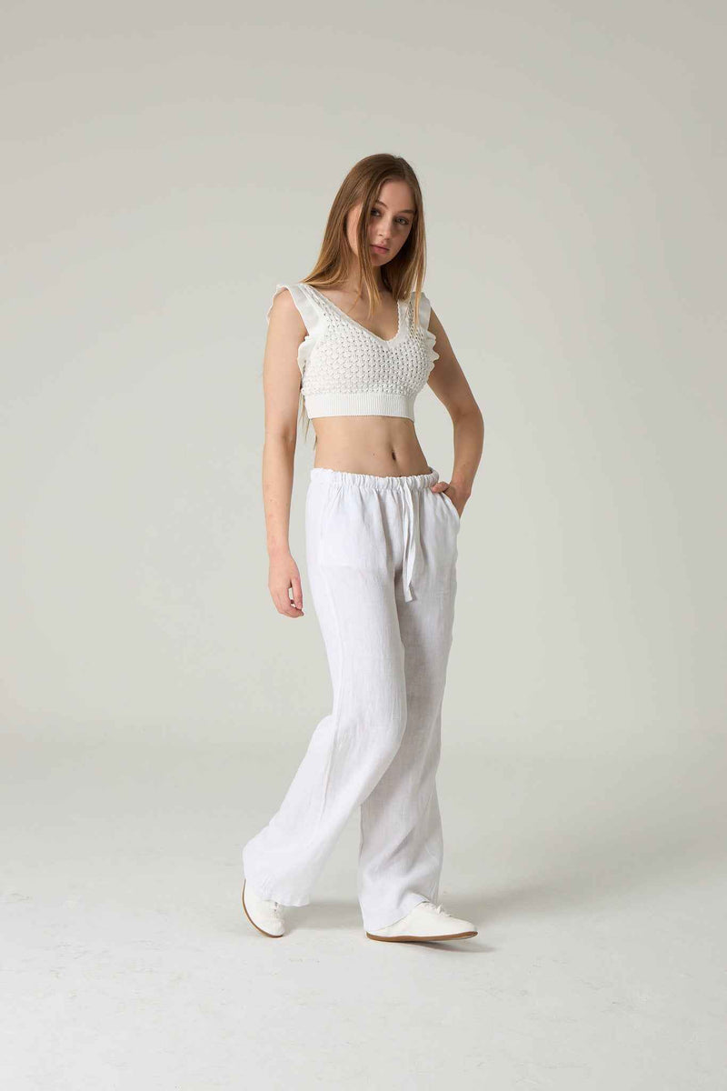 Woman wearing a white crochet top and white pants on a plain background.