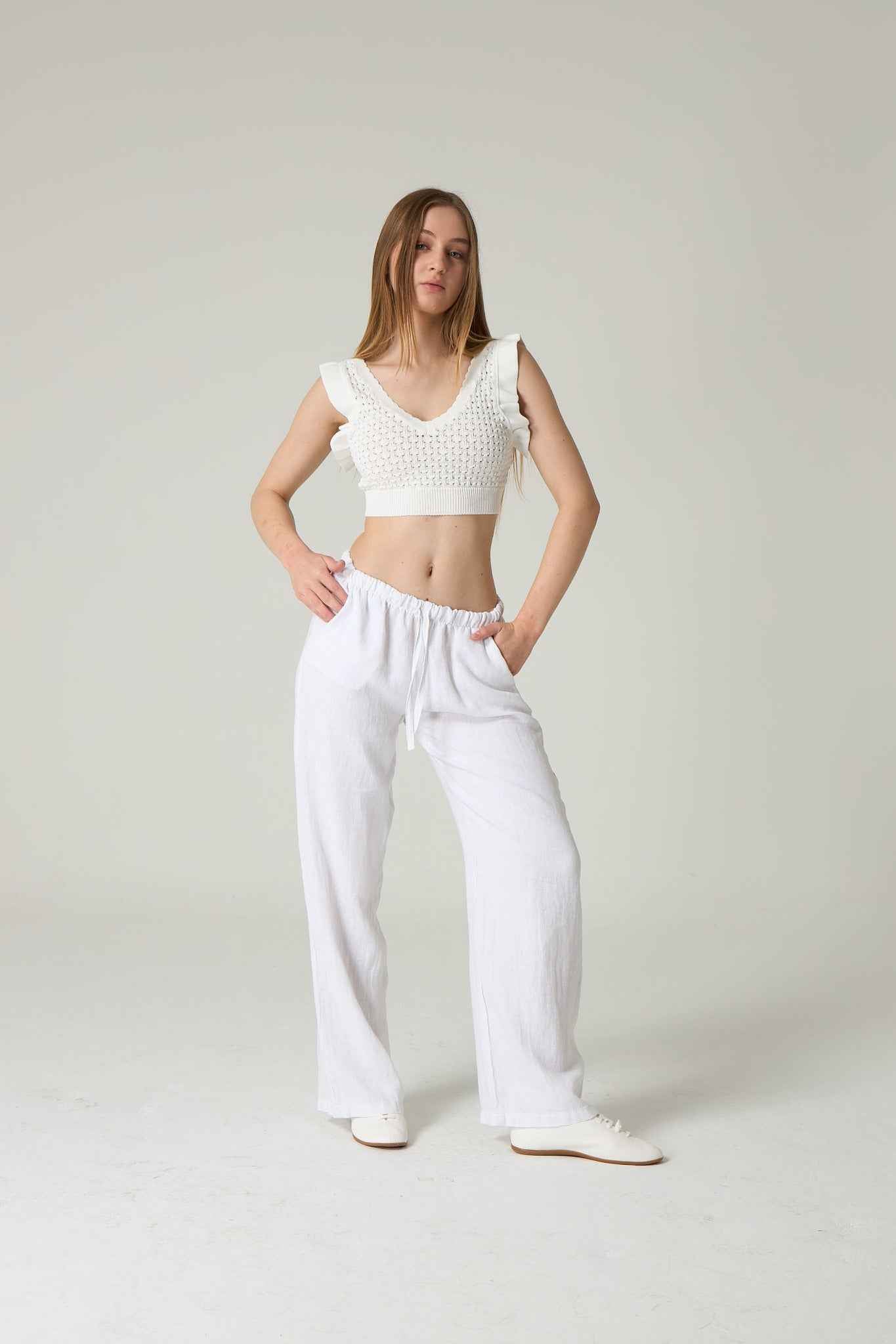 Woman wearing a white crochet top and white pants against a plain background.