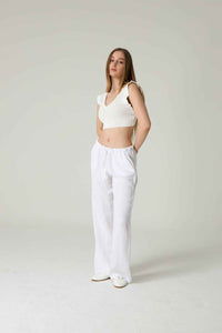 Woman wearing a white sleeveless top and white pants against a plain background.