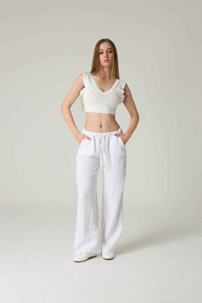 Woman wearing a white knit top and white pants on a plain background.