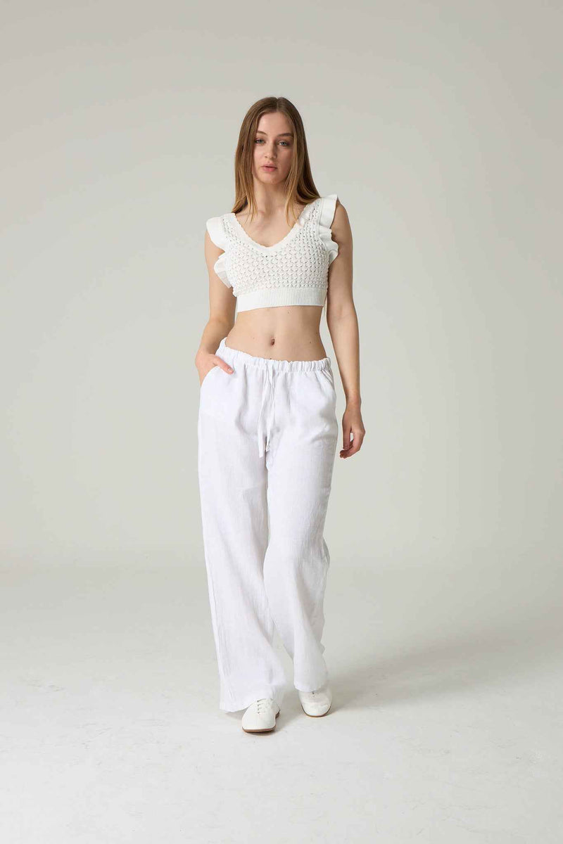Woman wearing a white crochet top and white pants on a plain background.