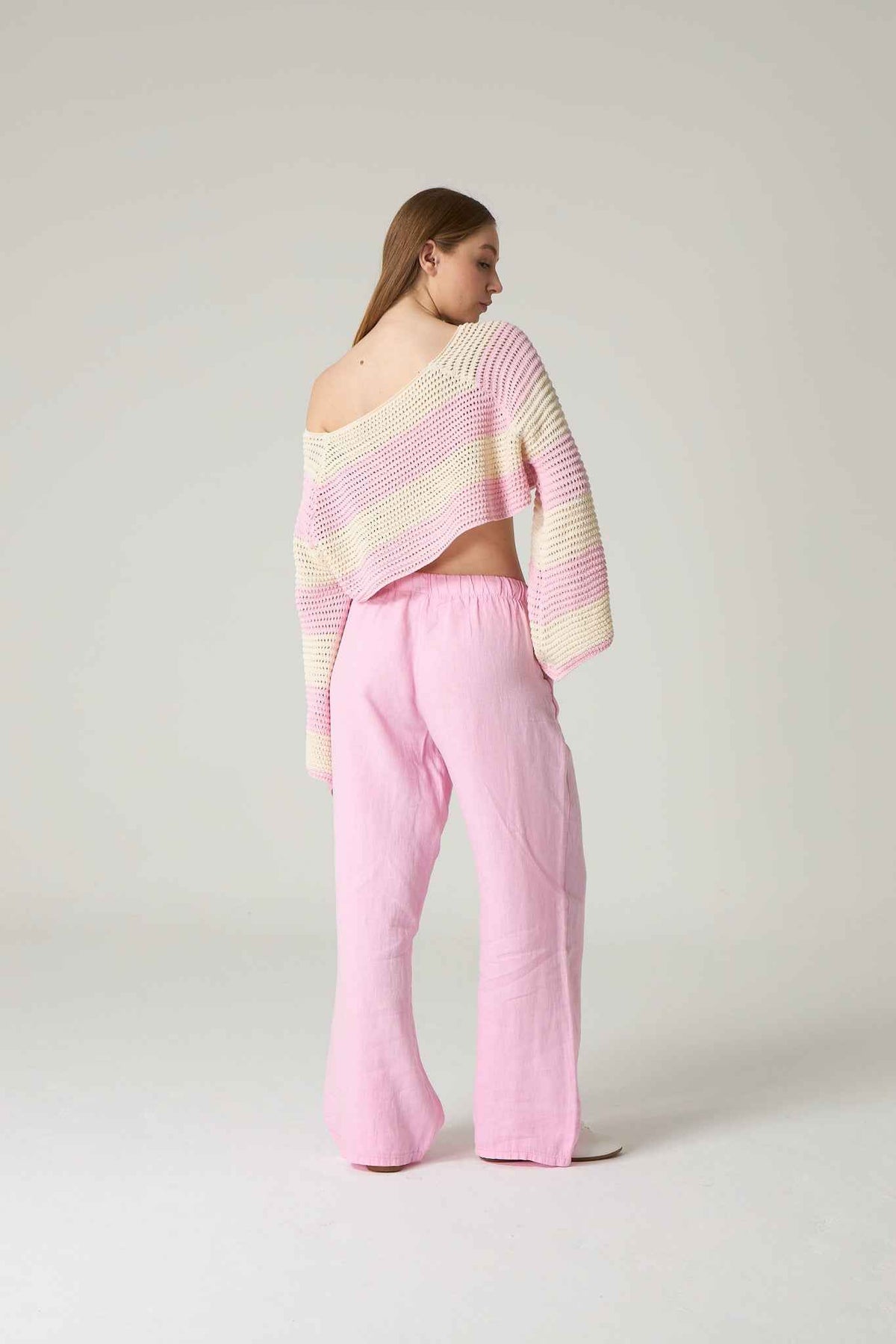 Woman wearing a pastel striped sweater and pink pants on a white background.