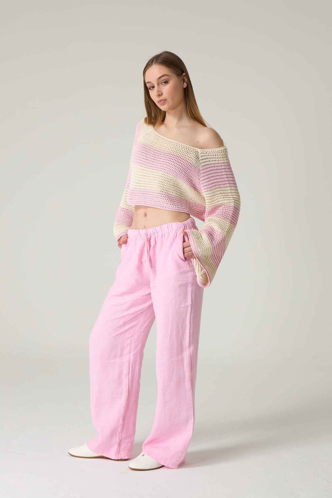 Woman wearing a striped off-shoulder top and pink pants on a plain background.