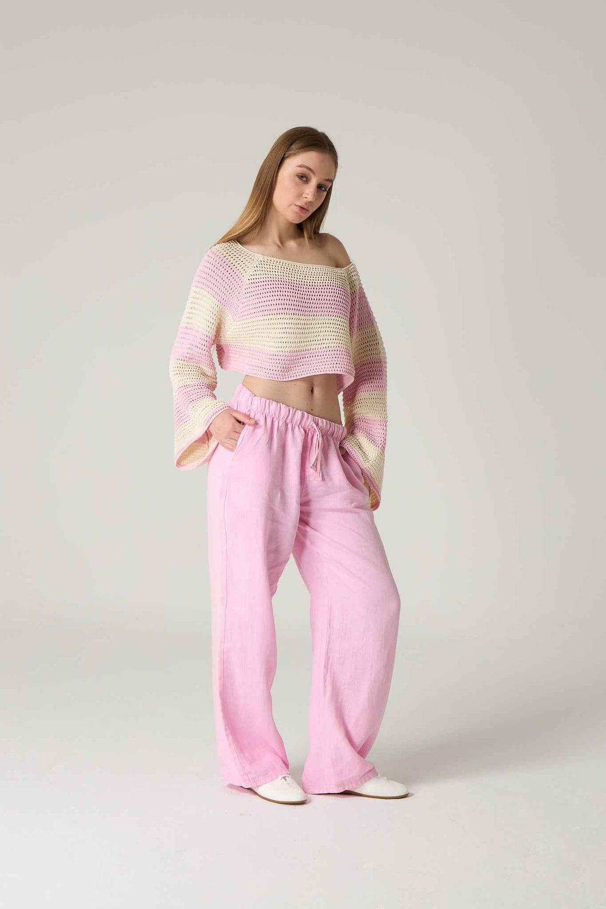 Woman wearing a colorful off-shoulder top and pink pants on a plain background.