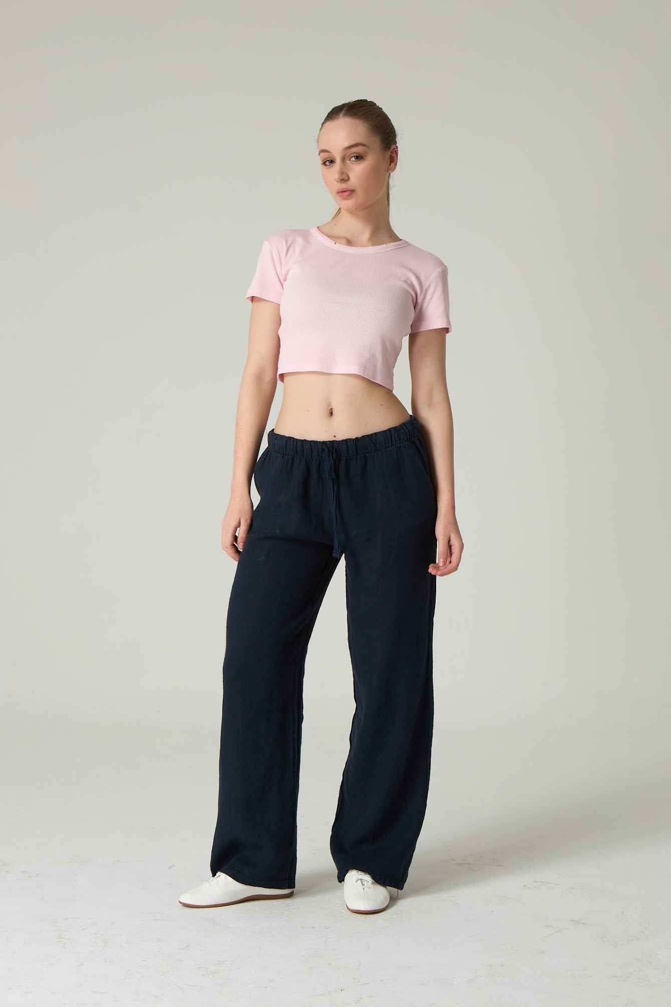 Woman wearing a pink crop top and black wide-leg pants on a plain background.
